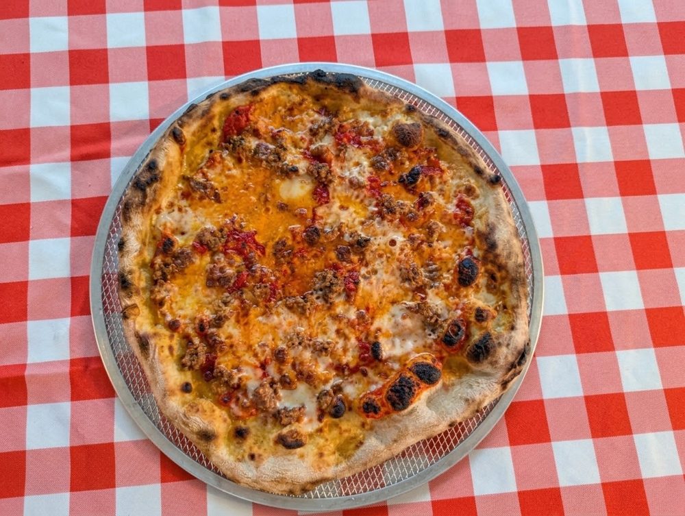 Pizza topped with sausage and red peppers on a checkered tablecloth